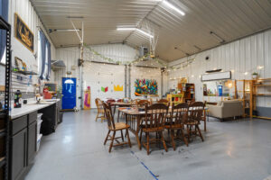 Interior of Simon Maker Studio in Viroqua, Wisconsin, showing large creative workspace with string lights, long tables, art supplies, colorful mural, and cozy seating area.